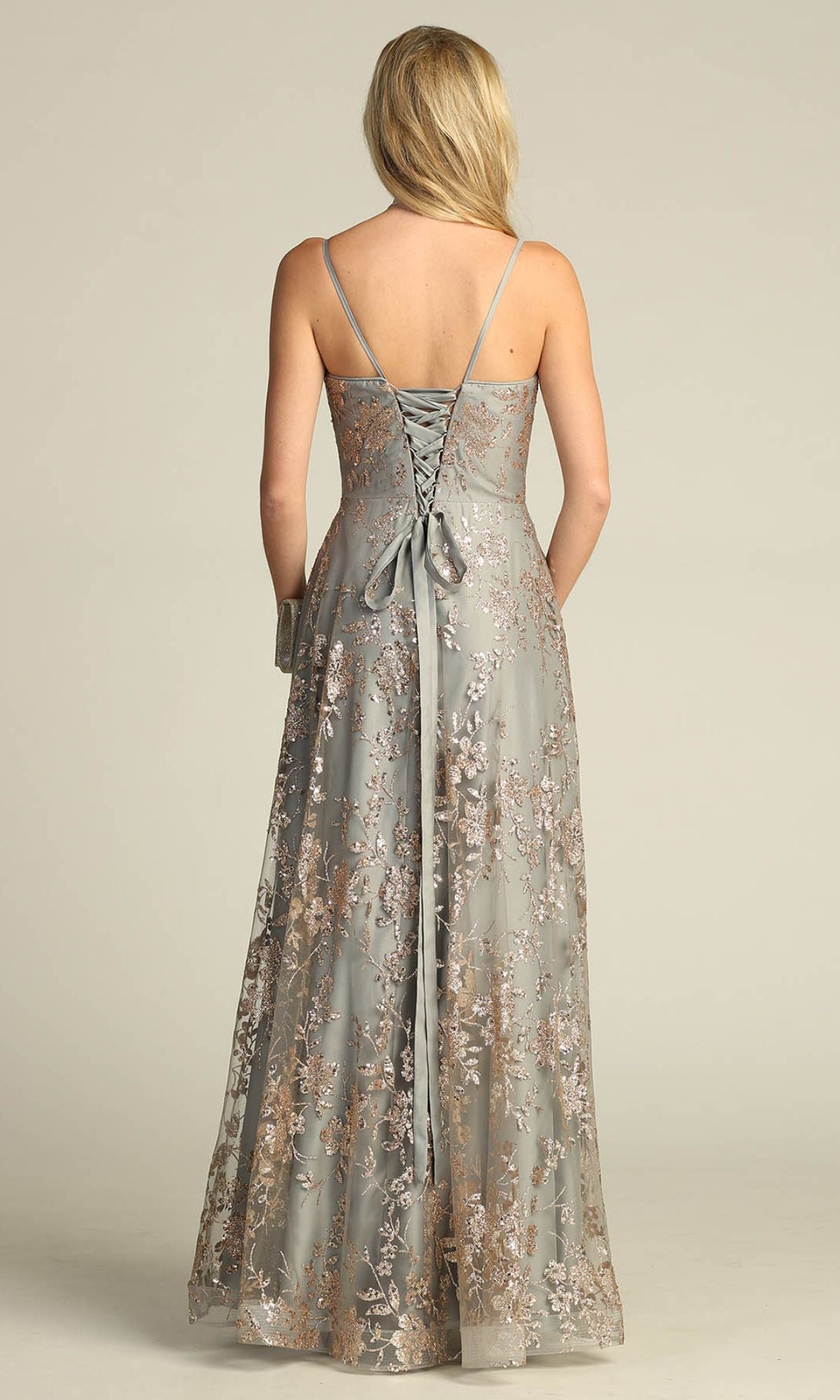 A woman faces away, wearing the Chicas C6534 Glitter-Print Long Gray Prom Dress with floral embroidery, thin straps, sparkling glitter print, and an elegant lace-up back.